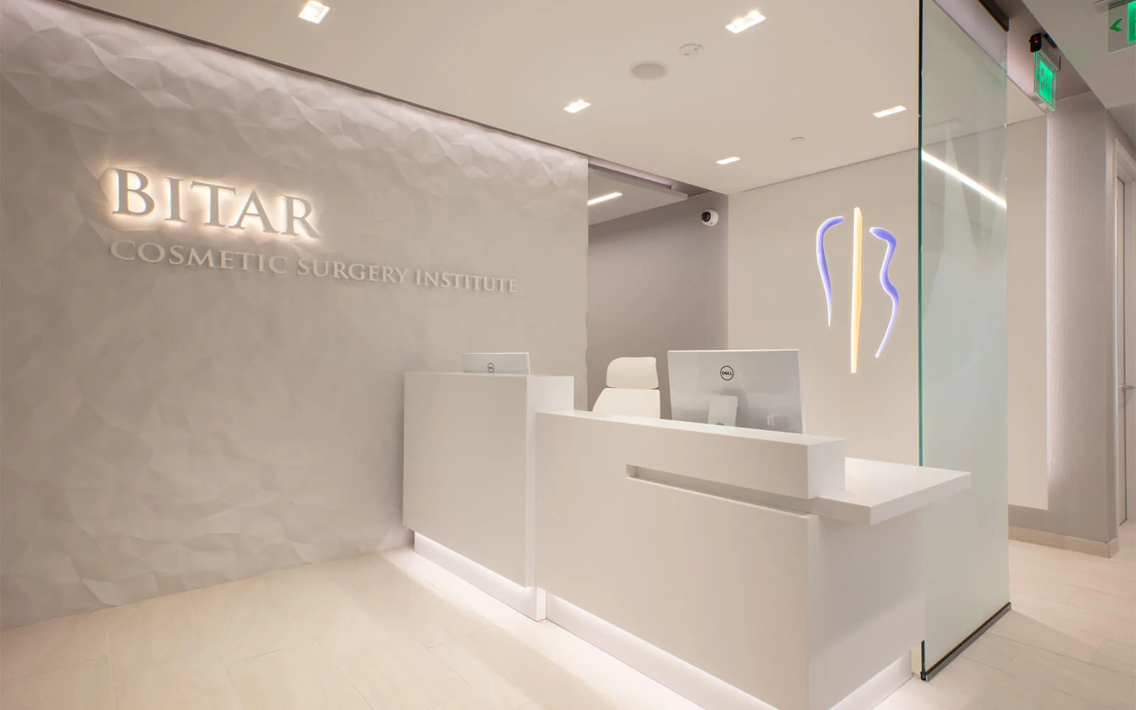 The modern, white reception area of the Bitar Cosmetic Surgery Institute, featuring a glowing logo on a textured wall and a neon silhouette sign.