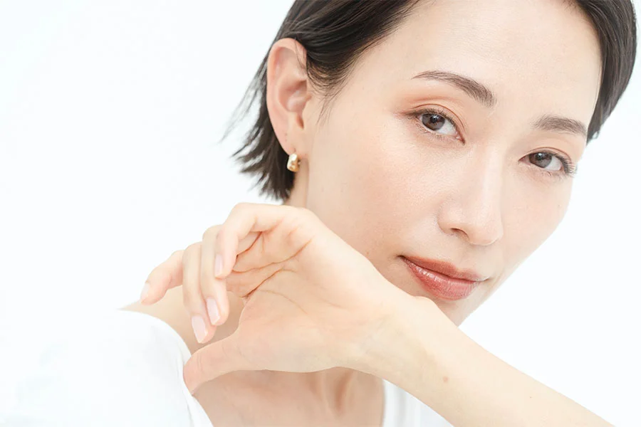 A close-up of a woman with short dark hair, wearing a white shirt and small gold hoop earrings. She is resting her chin on her hand and looking at the camera. The background is a solid white. - TRL in Fairfax, PA